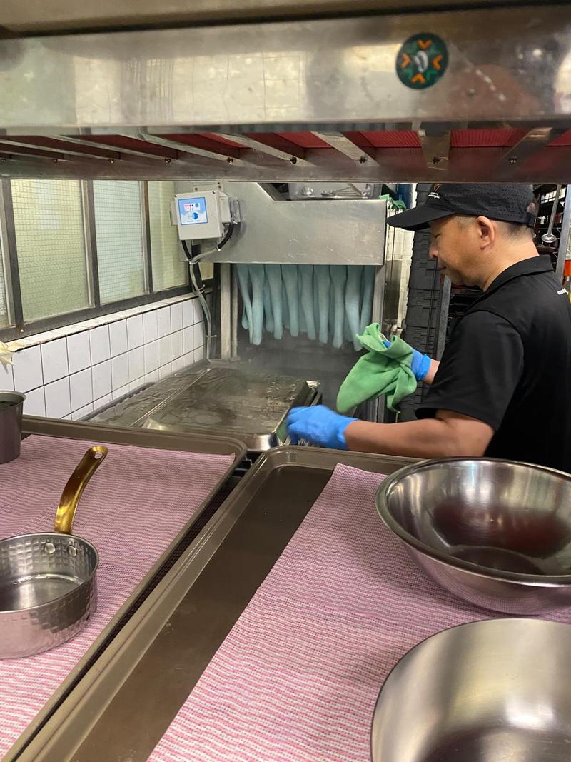 Dishwasher drying stainless steel bowls beside a conveyor dishwashing machine in a commercial kitchen