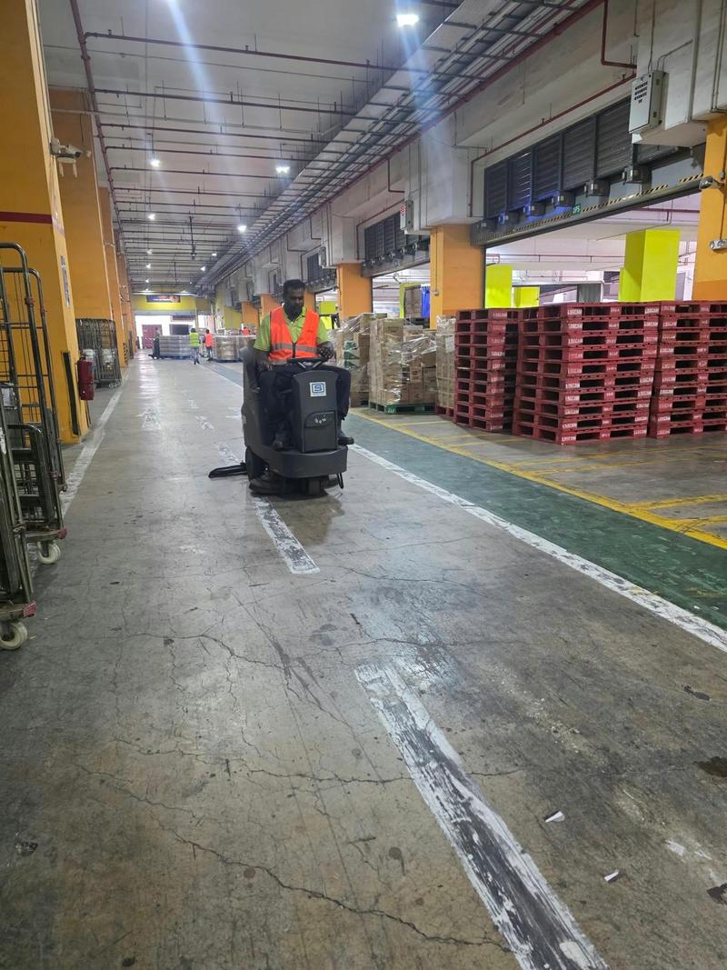 Ride-on floor scrubber cleaning a long warehouse aisle in a Singapore distribution centre